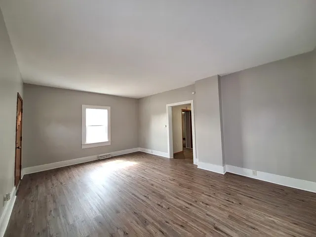 a view of an empty room with wooden floor and window