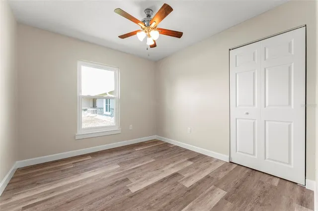 an empty room with wooden floor ceiling fan and windows