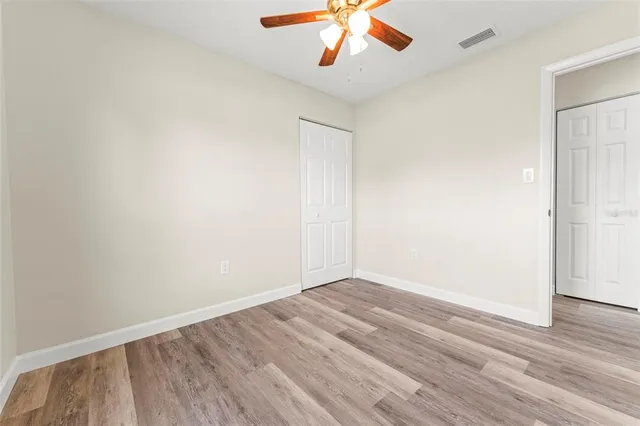 a view of an empty room with wooden floor and a ceiling fan