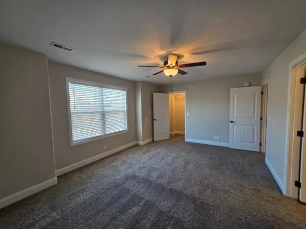 an empty room with chandelier fan and windows