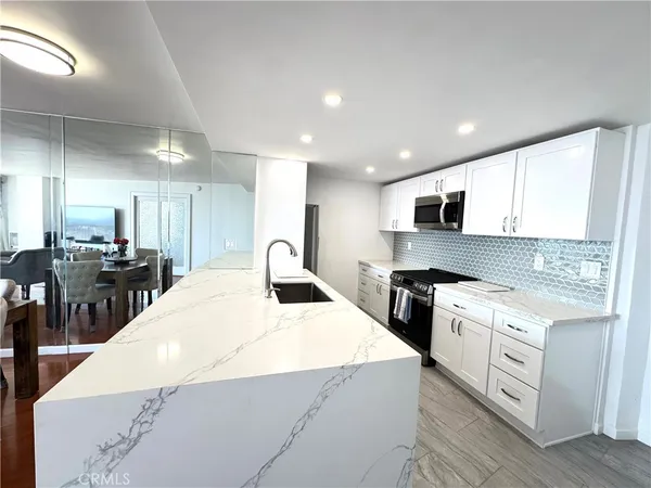 a kitchen with stainless steel appliances kitchen island granite countertop a stove a sink a refrigerator and white cabinets with wooden floor