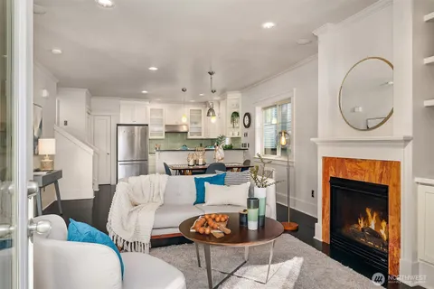 a living room with stainless steel appliances furniture a fireplace and a kitchen view