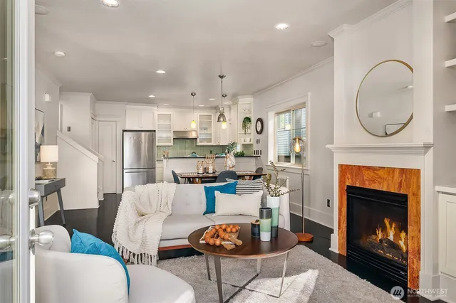 a living room with stainless steel appliances furniture a fireplace and a kitchen view