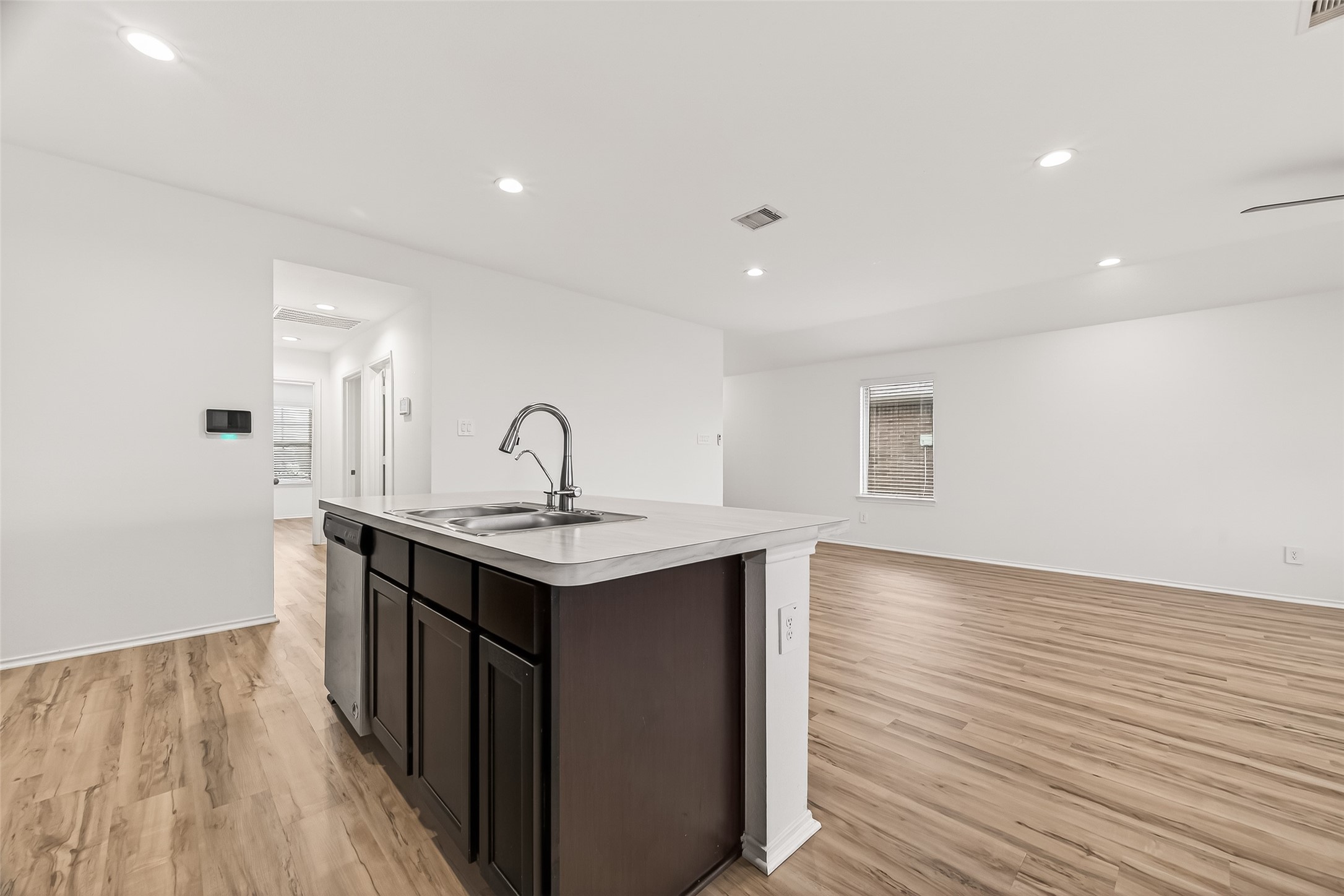 21522 Violet Ridge Road Katy, TX 77449 - Photo 14 of 39 This modern kitchen features a spacious open layout with light wood flooring and recessed lighting. The central island includes a sleek sink and dark cabinetry, providing a stylish contrast. The area extends into a bright, airy living space, perfect for entertaining.