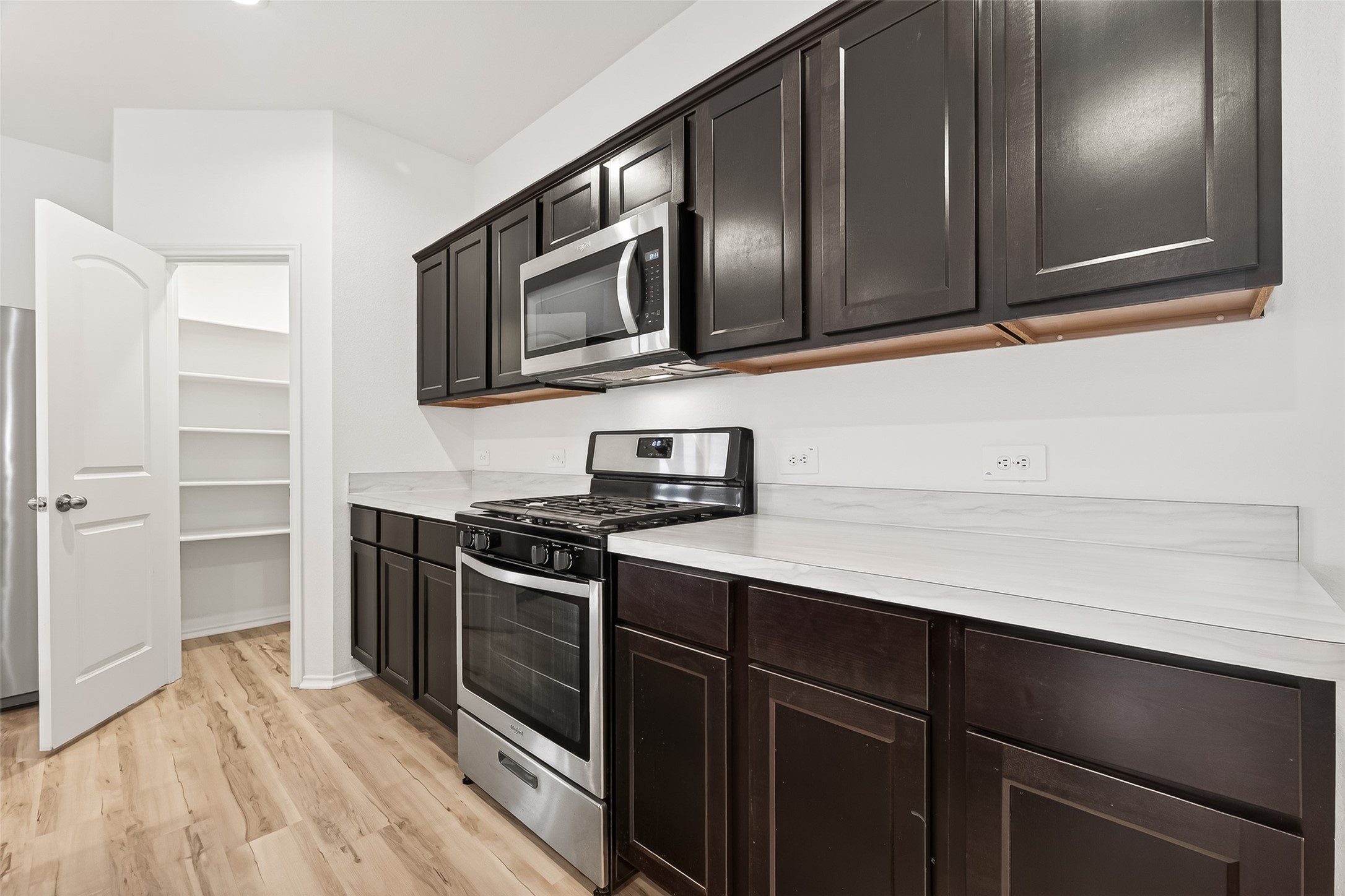21522 Violet Ridge Road Katy, TX 77449 - Photo 15 of 39 Modern kitchen with dark wood cabinets, stainless steel appliances, and a gas range. Features a spacious pantry and light wood flooring, offering a sleek, functional space.
