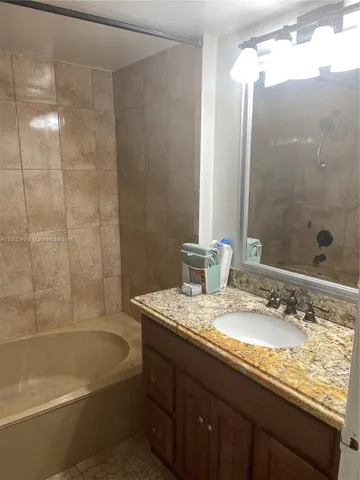 a bathroom with a granite countertop bathtub shower sink vanity and toilet