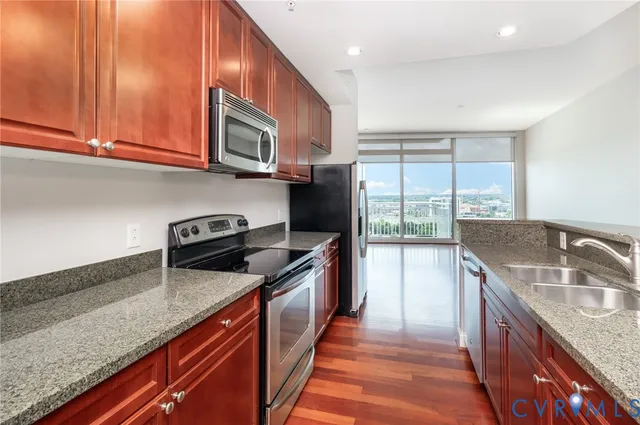 a kitchen with granite countertop stainless steel appliances a sink dishwasher a stove top oven a refrigerator with wooden cabinets and floor