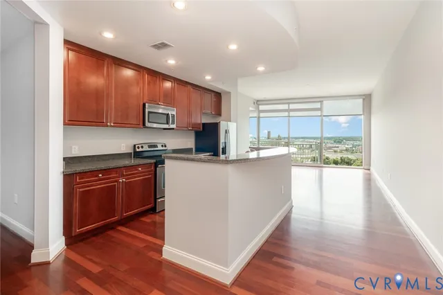a kitchen with stainless steel appliances granite countertop a stove top oven a sink dishwasher a microwave oven and a refrigerator with wooden floor