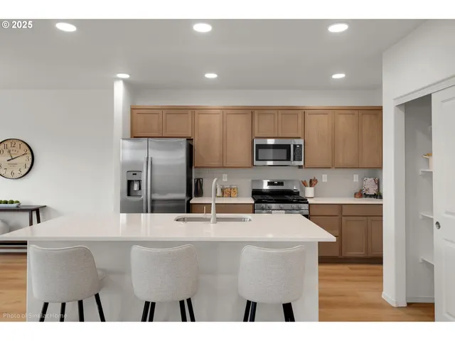 a kitchen with stainless steel appliances kitchen island granite countertop a stove a sink a refrigerator and white cabinets with wooden floor