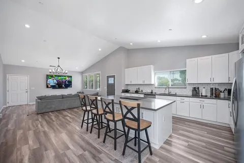 a kitchen with stainless steel appliances kitchen island granite countertop a stove a sink a dining table and chairs with wooden floor