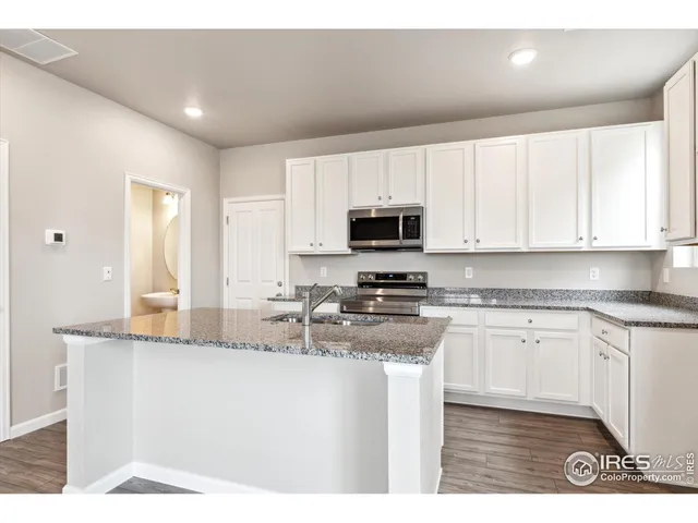 a kitchen with kitchen island granite countertop a sink a stove a microwave and wooden cabinets