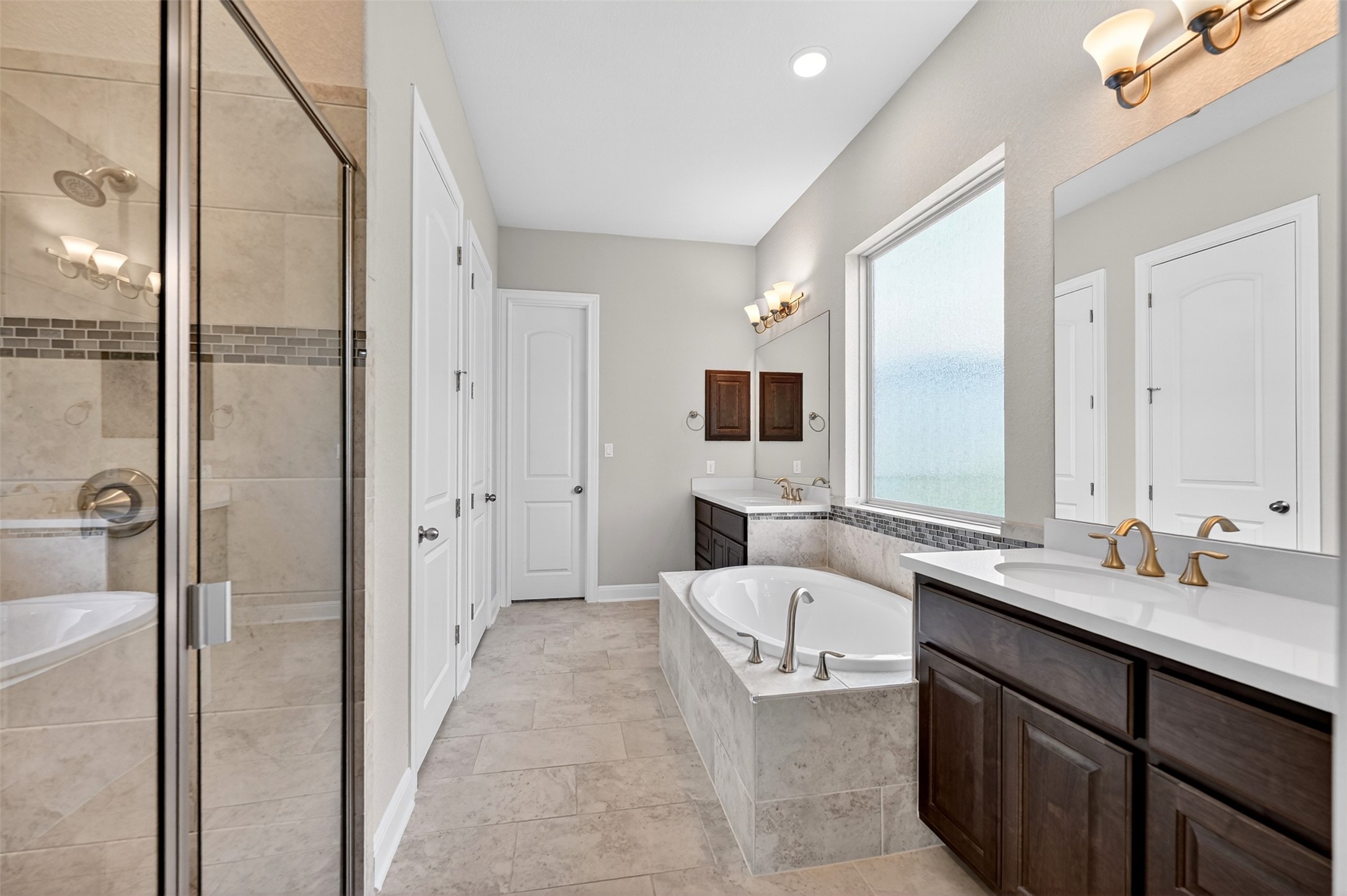 1201 Positano Pass Leander, TX 78641 - Photo 25 of 40 Spacious bathroom featuring a built-in soaking tub, dual vanity sinks with white countertops, dark wood-finish cabinetry, and a glass-enclosed shower with tile surround