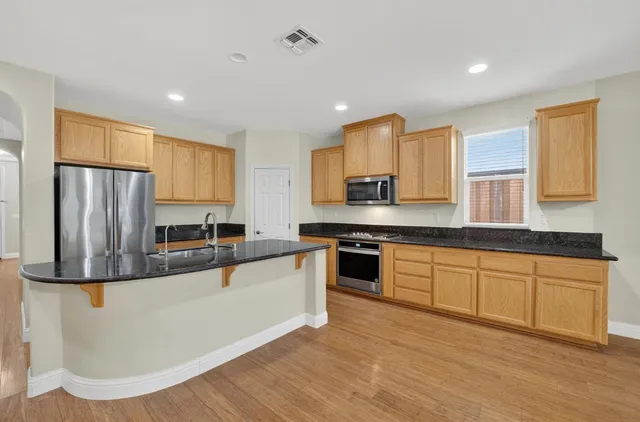 a large kitchen with stainless steel appliances granite countertop a stove a sink a refrigerator and white cabinets with wooden floor