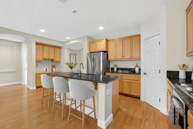 a kitchen with stainless steel appliances granite countertop a stove a sink a refrigerator white cabinets and wooden floor