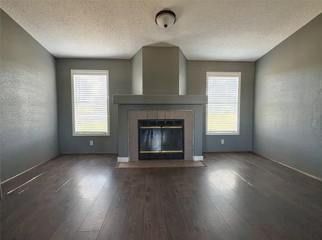 an empty room with wooden floor fireplace and windows