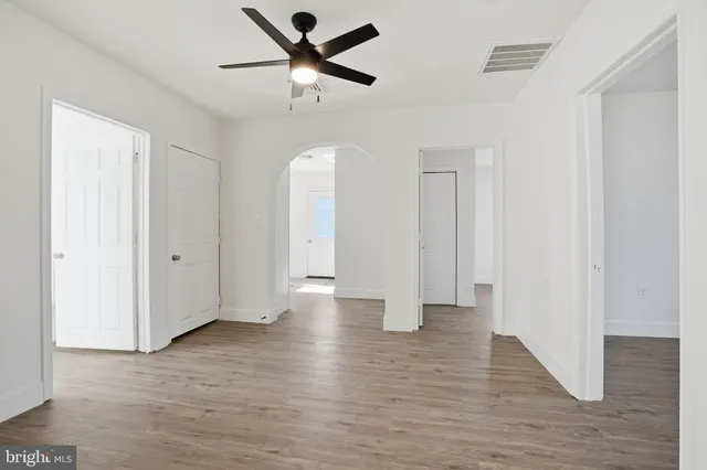 a view of an empty room with wooden floor and a ceiling fan