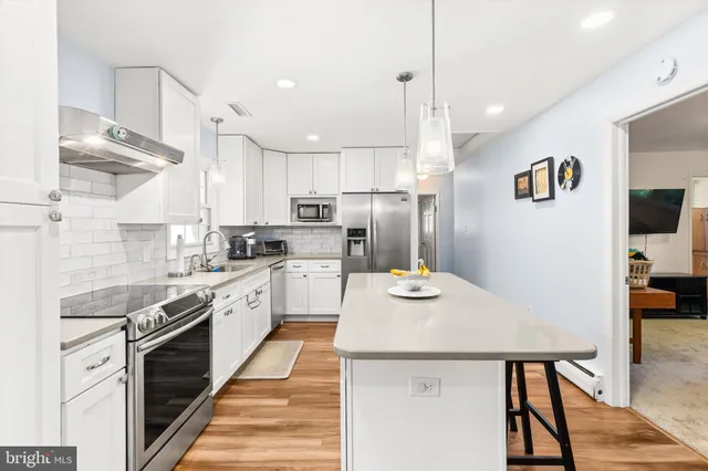 a kitchen with stainless steel appliances a stove a sink dishwasher a refrigerator white cabinets and wooden floor next to a window