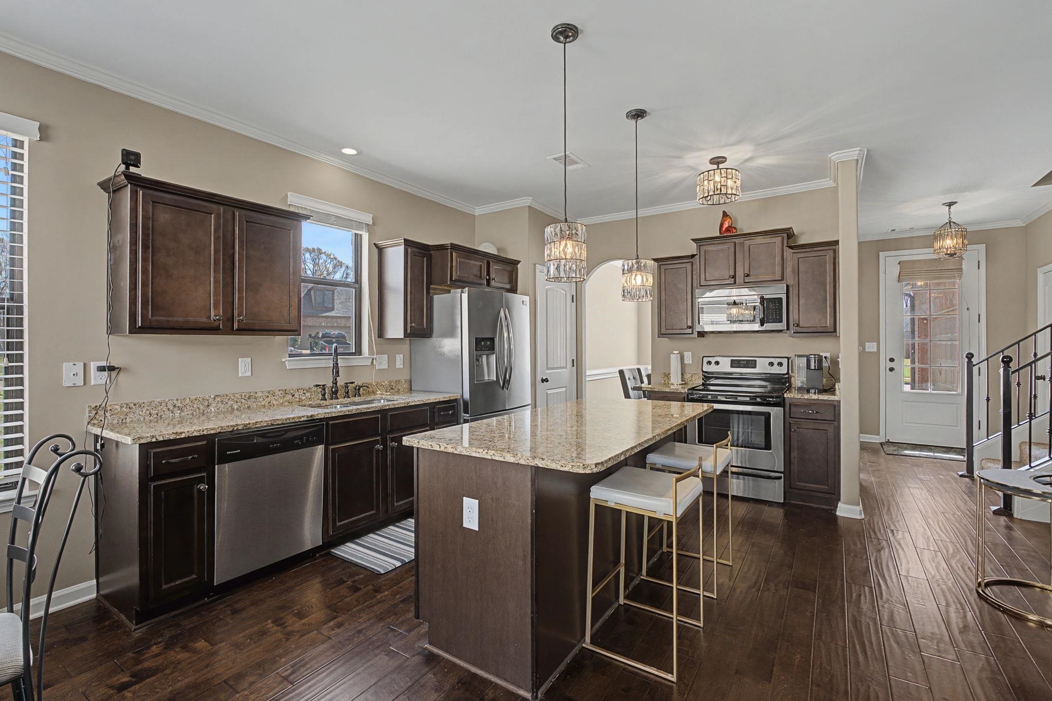 12436 Dusty Field Road Arlington, TN 38002 - Photo 12 of 40 Kitchen featuring dark wood finish cabinetry, stainless steel appliances, ornamental molding, a kitchen island, and light stone countertops