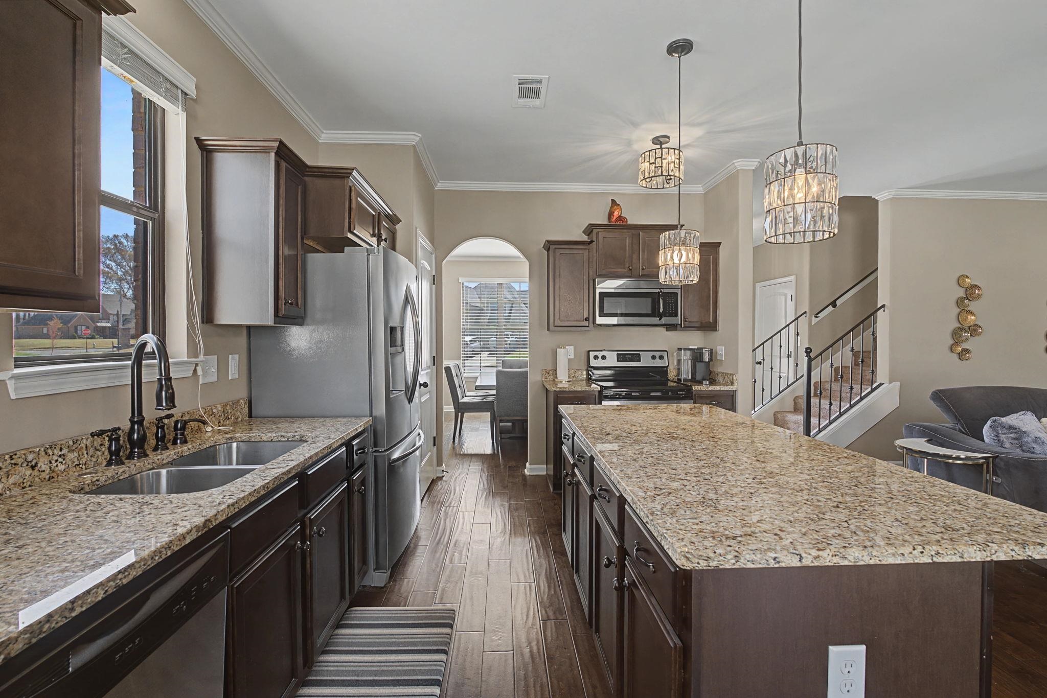 12436 Dusty Field Road Arlington, TN 38002 - Photo 13 of 40 Kitchen featuring dark wood finish cabinetry, light stone countertops, arched walkways, stainless steel appliances, and crown molding