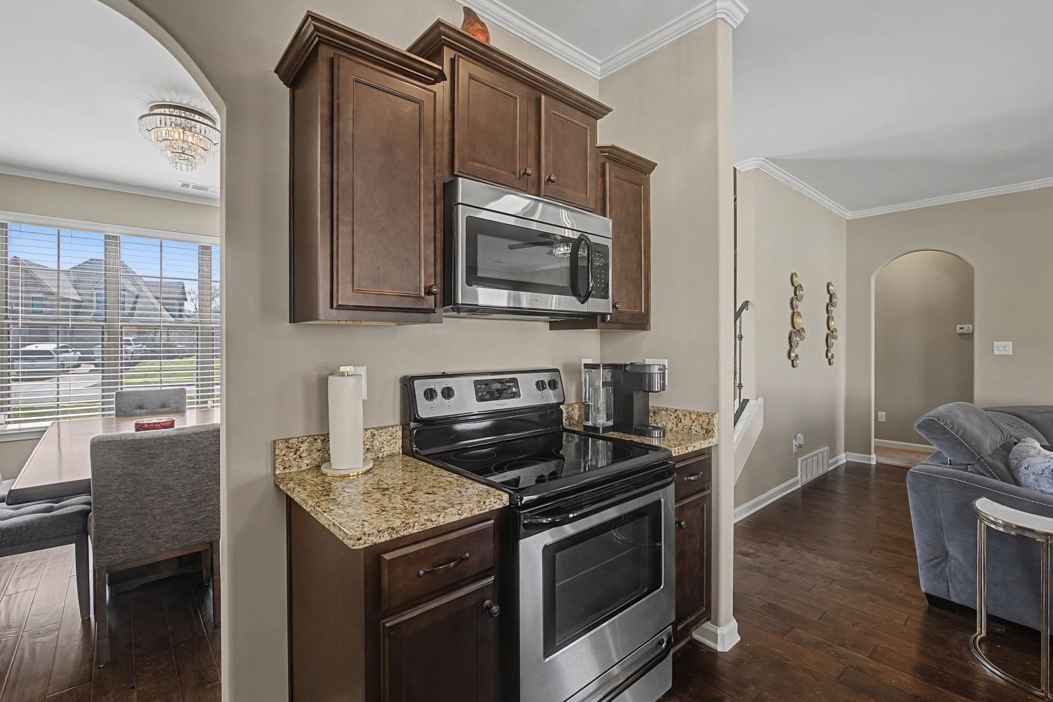 12436 Dusty Field Road Arlington, TN 38002 - Photo 15 of 40 Kitchen with arched walkways, stainless steel appliances, dark wood finish cabinetry, crown molding, and light stone counters