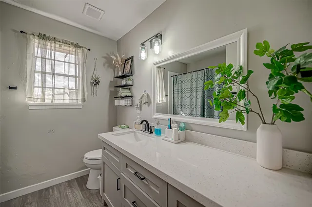 a bathroom with a granite countertop sink a toilet a window and shower