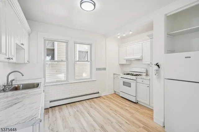 a kitchen with a refrigerator stove and white cabinets with wooden floor