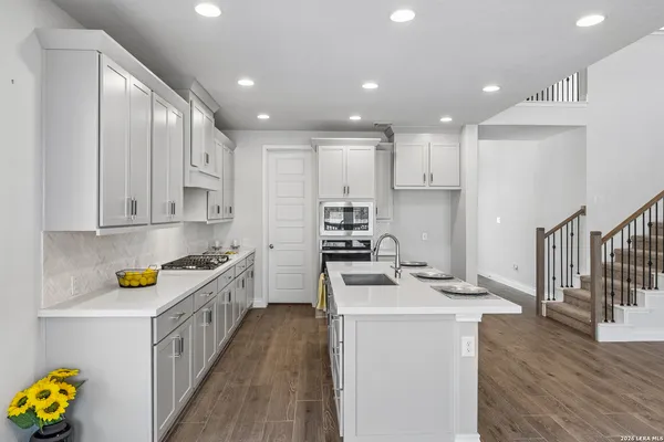 a kitchen with stainless steel appliances a stove a sink a refrigerator white cabinets and wooden floor