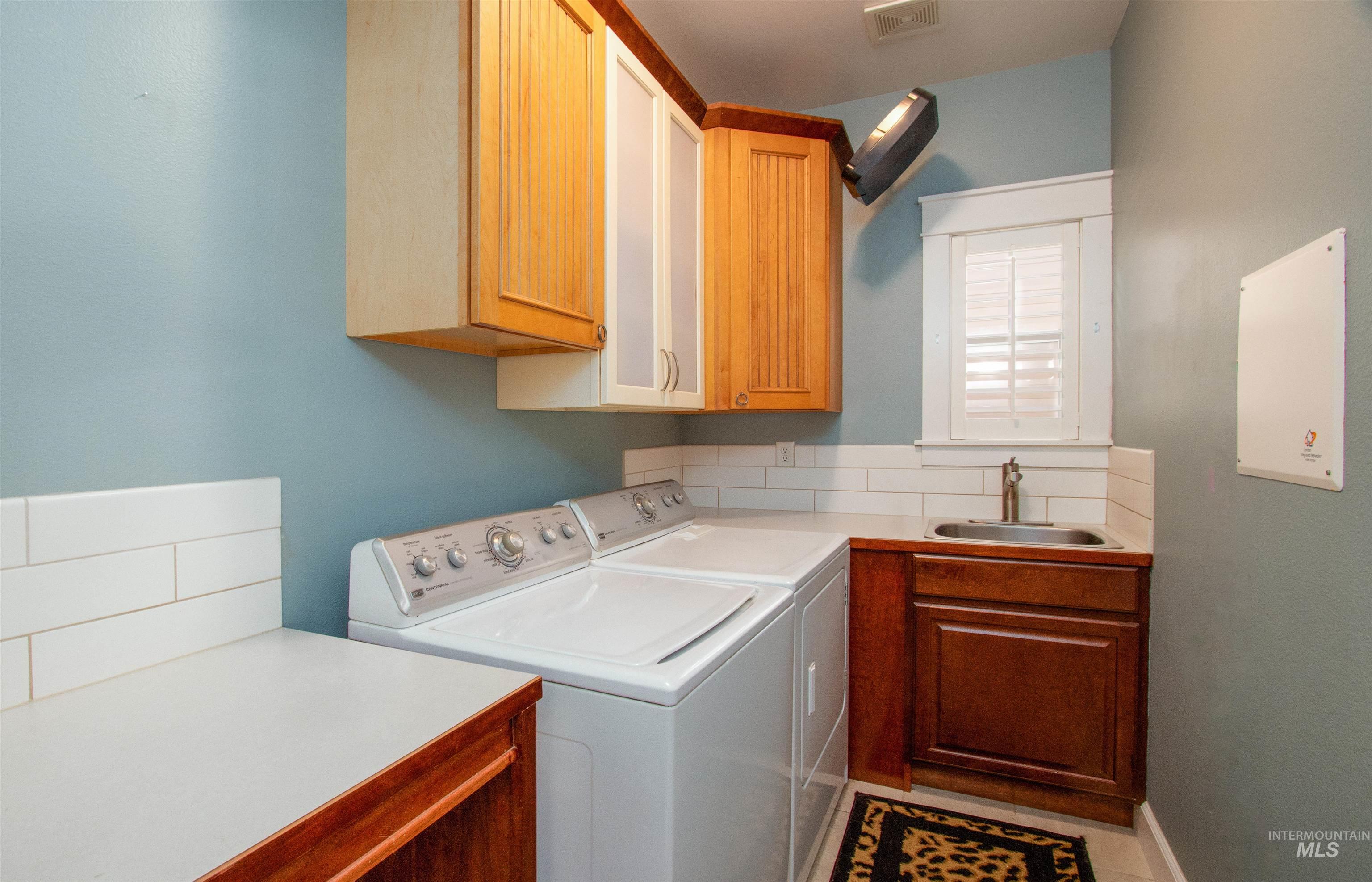 892 South Capitola Way Boise, ID 83712 - Photo 18 of 34 Dedicated laundry area featuring a utility sink, wood-finish cabinetry, white subway tile backsplash, and a window with white louvered shutters