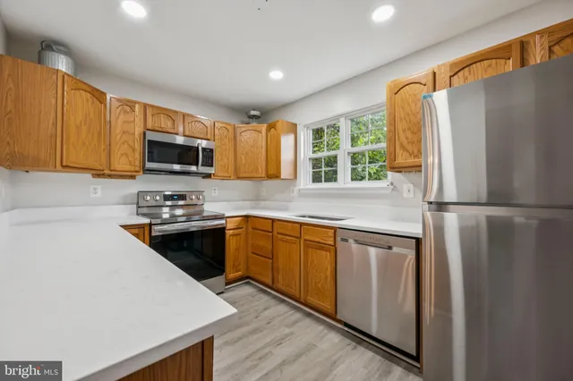 a kitchen with stainless steel appliances granite countertop a refrigerator a stove top oven a sink dishwasher and wooden cabinets with wooden floor