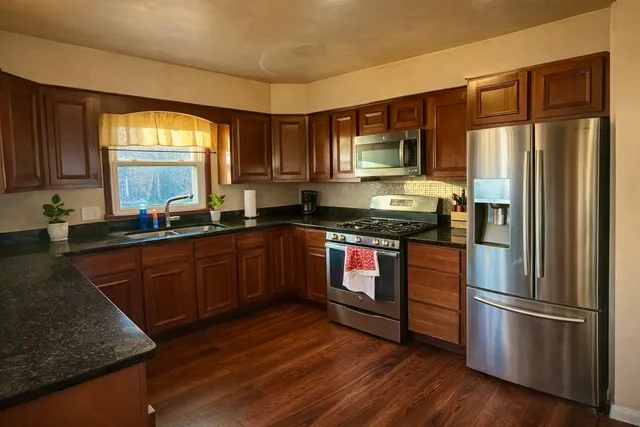 a kitchen with granite countertop wooden floors stainless steel appliances a sink and a window