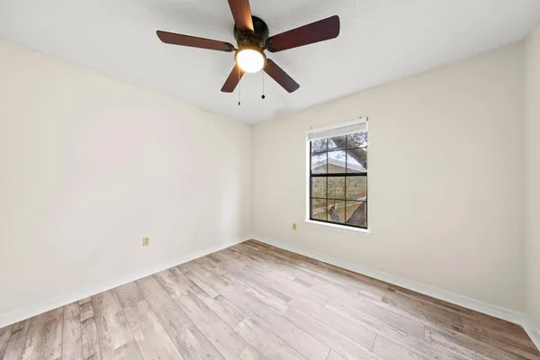 an empty room with wooden floor ceiling fan and windows