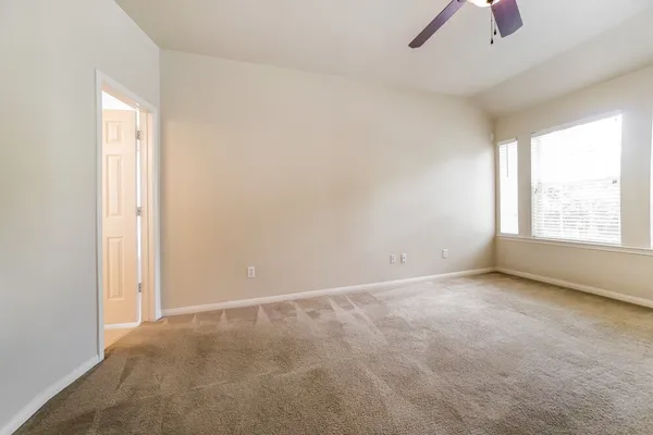 an empty room with chandelier fan and windows