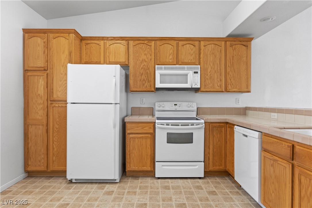 1430 Star Road Pahrump, NV 89048 - Photo 22 of 32 Kitchen with white appliances, tile counters, lofted ceiling, and brown cabinets