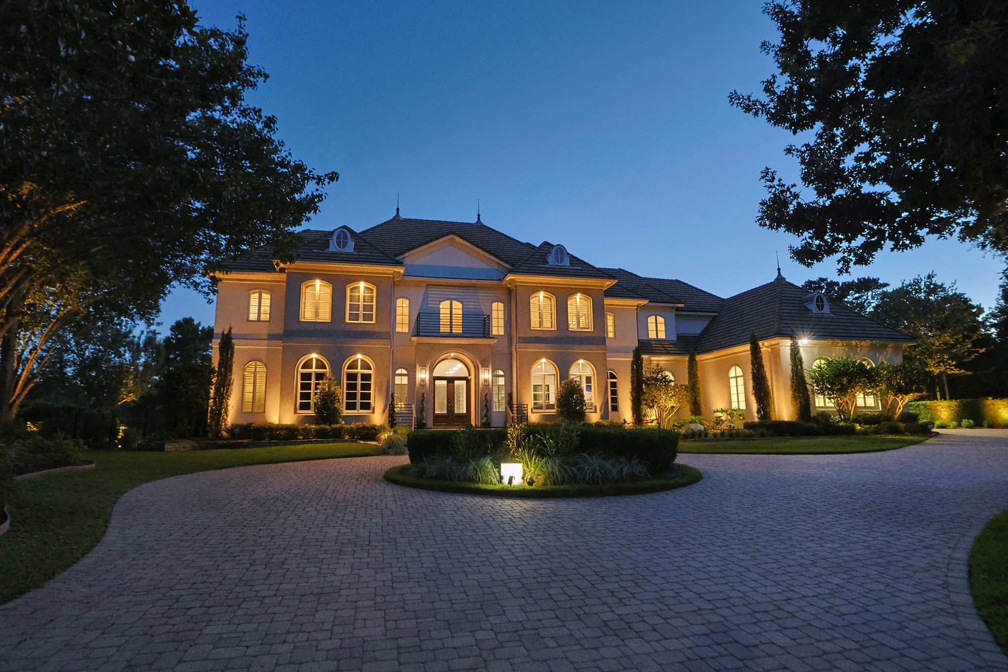 39 Maymont Way Spring, TX 77382 - Photo 46 of 50 This elegant two-story home features a grand facade with warm exterior lighting, a spacious driveway, and lush landscaping, creating a welcoming and luxurious atmosphere.