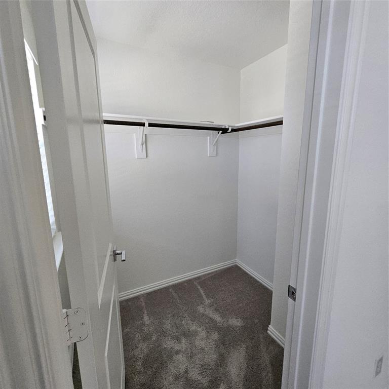 2309 Jack Rabbit Way Northlake, TX 76247 - Photo 18 of 28 Spacious walk-in closet featuring white painted walls, a dark brown clothing rod with white supports, and gray carpet flooring