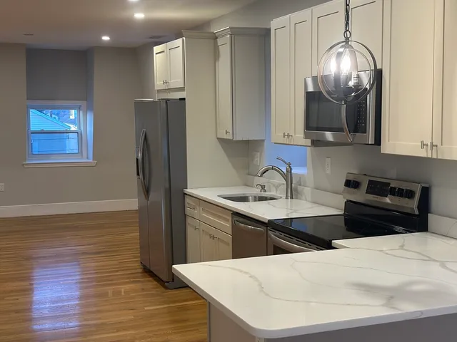 a kitchen with stainless steel appliances kitchen island granite countertop a refrigerator a sink a stove and wooden floor