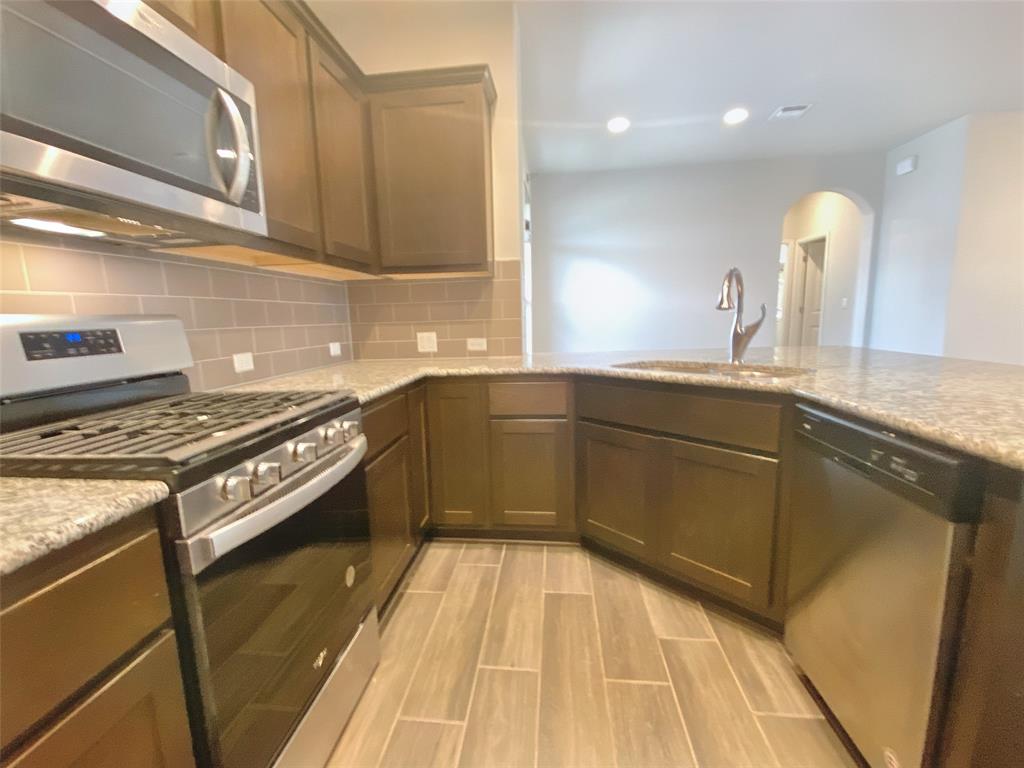 8901 Panhandle Drive Austin, TX 78747 - Photo 10 of 21 Kitchen featuring granite countertops, wood-finish flooring, stainless steel appliances, dark wood cabinetry, and a subway tile backsplash