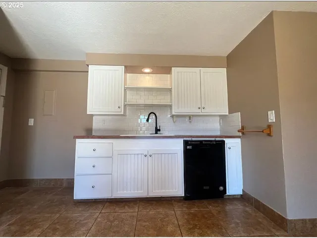 a white kitchen with a sink and dishwasher a stove top oven with wooden floor