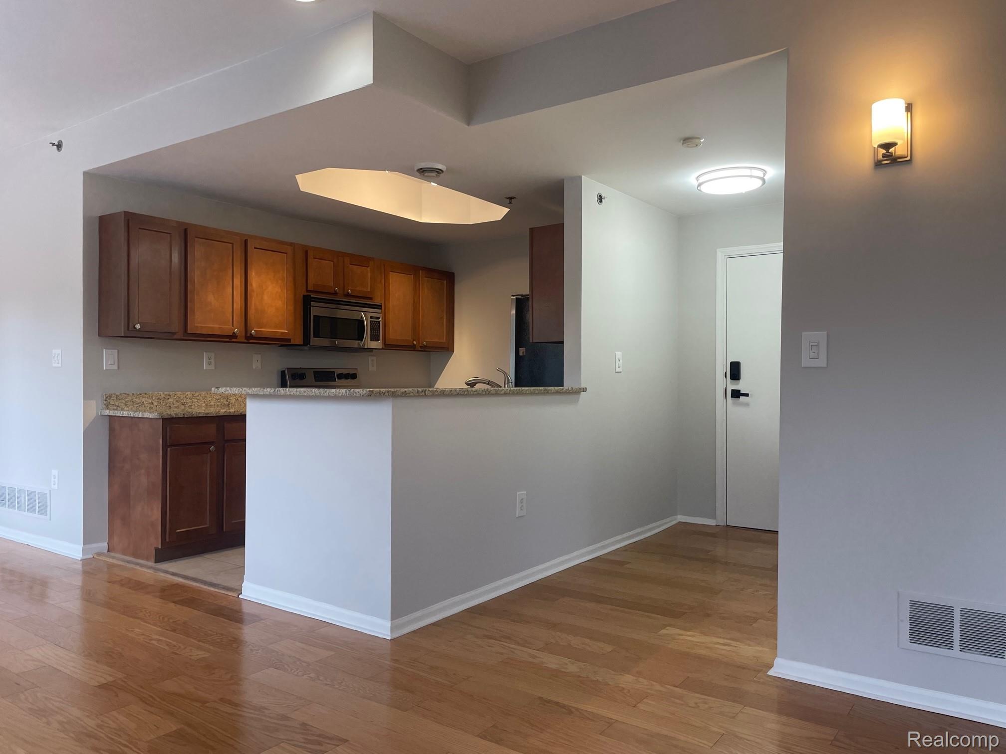 2727 East Maple Road Birmingham, MI 48009 - Photo 16 of 29 Wood-finish flooring throughout, kitchen featuring brown cabinetry, granite-finish countertops, and a stainless steel microwave
