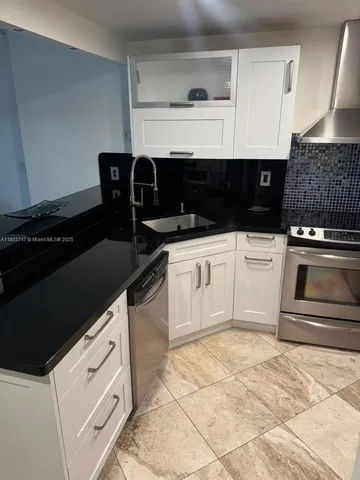 a kitchen with granite countertop a stove a sink and white cabinets