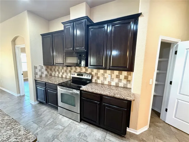 a kitchen with granite countertop a refrigerator and a stove top oven