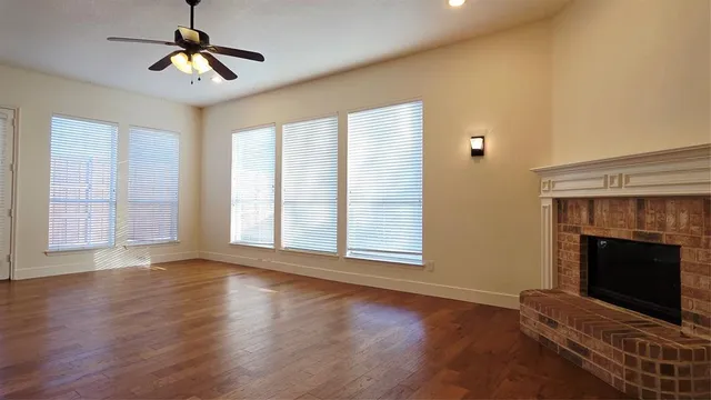 a view of an empty room with wooden floor fireplace and a window