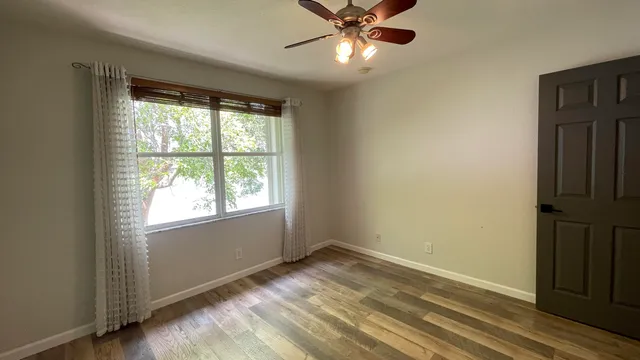 an empty room with wooden floor ceiling fan and windows
