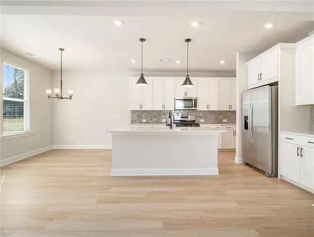 a view of kitchen with stainless steel appliances granite countertop kitchen island sink refrigerator and white cabinets
