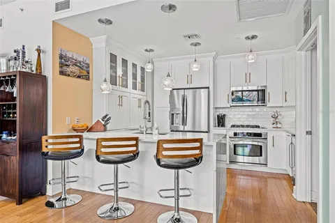 a kitchen with stainless steel appliances granite countertop a refrigerator a stove a sink counter tops and chairs with wooden floor