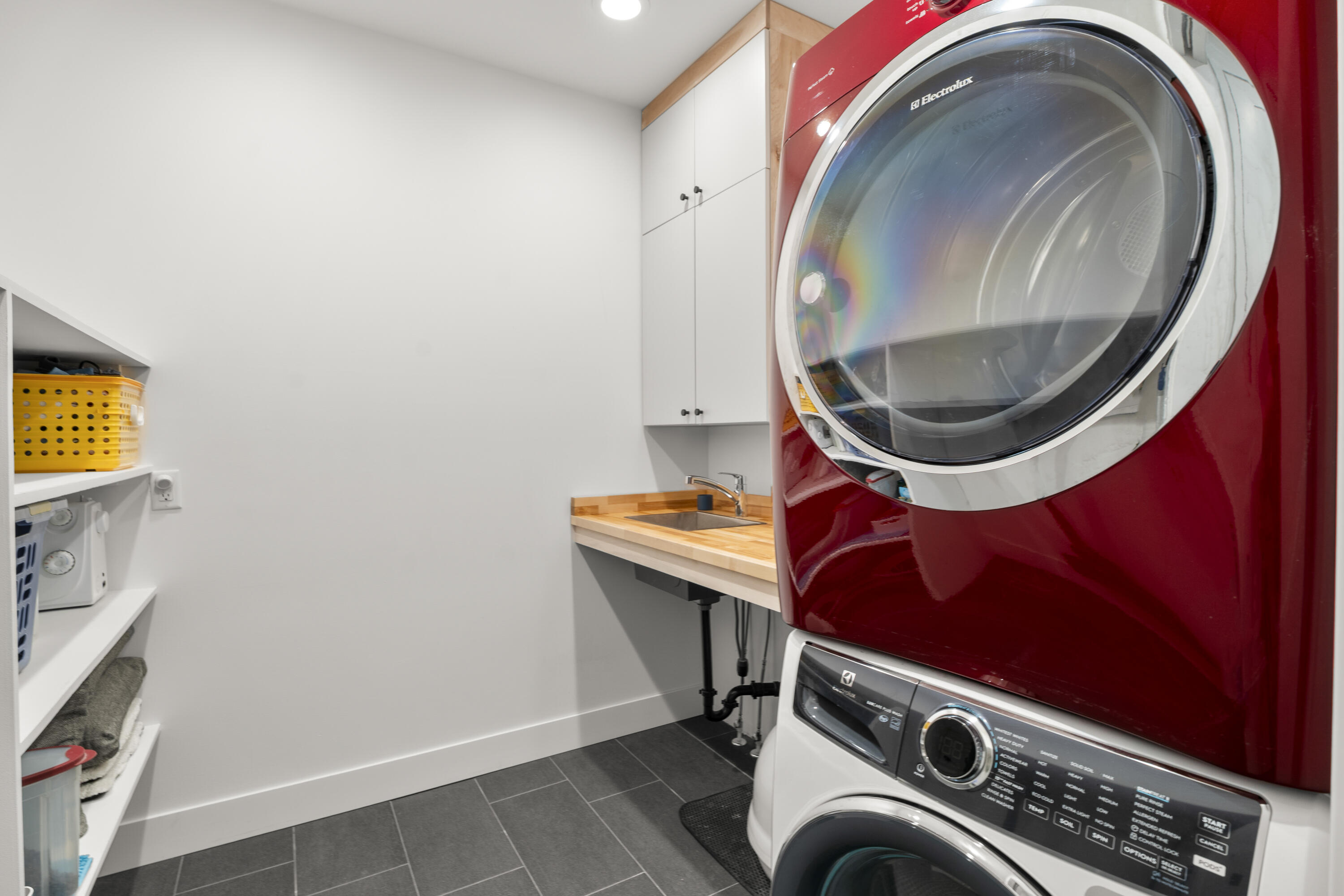 56670 Sunstone Loop, Unit LOT 141 Bend, OR 97707 - Photo 22 of 62 Functional laundry room with Electrolux washer and dryer, painted maple cabinetry, butcher block countertop, stainless utility sink, built-in shelving, and tile floors.