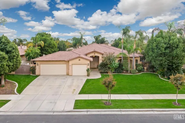 a white house with a yard plants and large tree