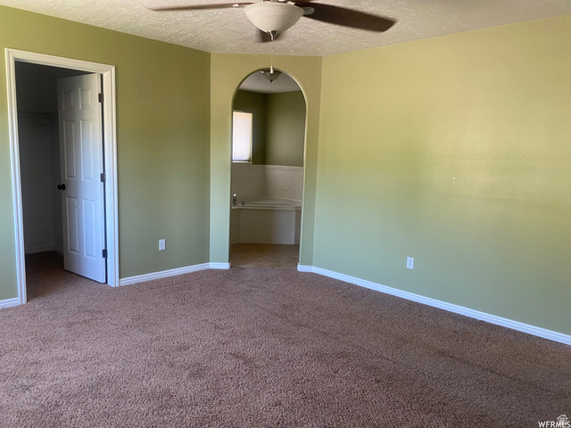 83 Canterbury Circle Logan, UT 84321 - Photo 13 of 23 Unfurnished bedroom featuring arched walkways, carpet flooring, a walk in closet, a textured ceiling, and ceiling fan