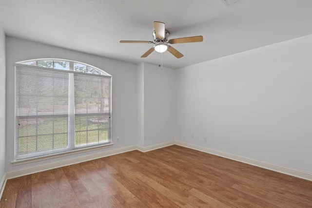 an empty room with wooden floor fan and windows