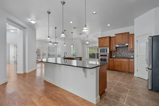 a large kitchen with stainless steel appliances kitchen island granite countertop a refrigerator a oven a sink and a stove